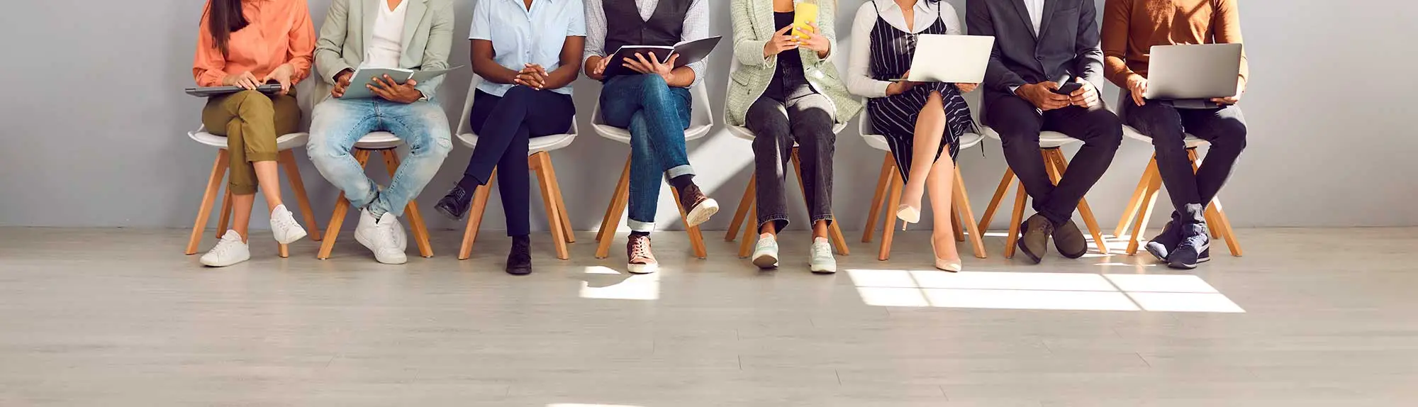 A diverse group of individuals sitting on chairs with laptops in front of them.